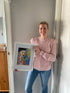 An photograph of a smiling woman holding a limited edition print titled "Pain", which features an abstract portrait of a woman in bold brushstrokes of blues and yellows.